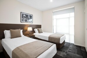 Habitación de hotel con dos camas, una mesita de noche con lámpara, un cuadro enmarcado en la pared y un amplio ventanal con vistas.