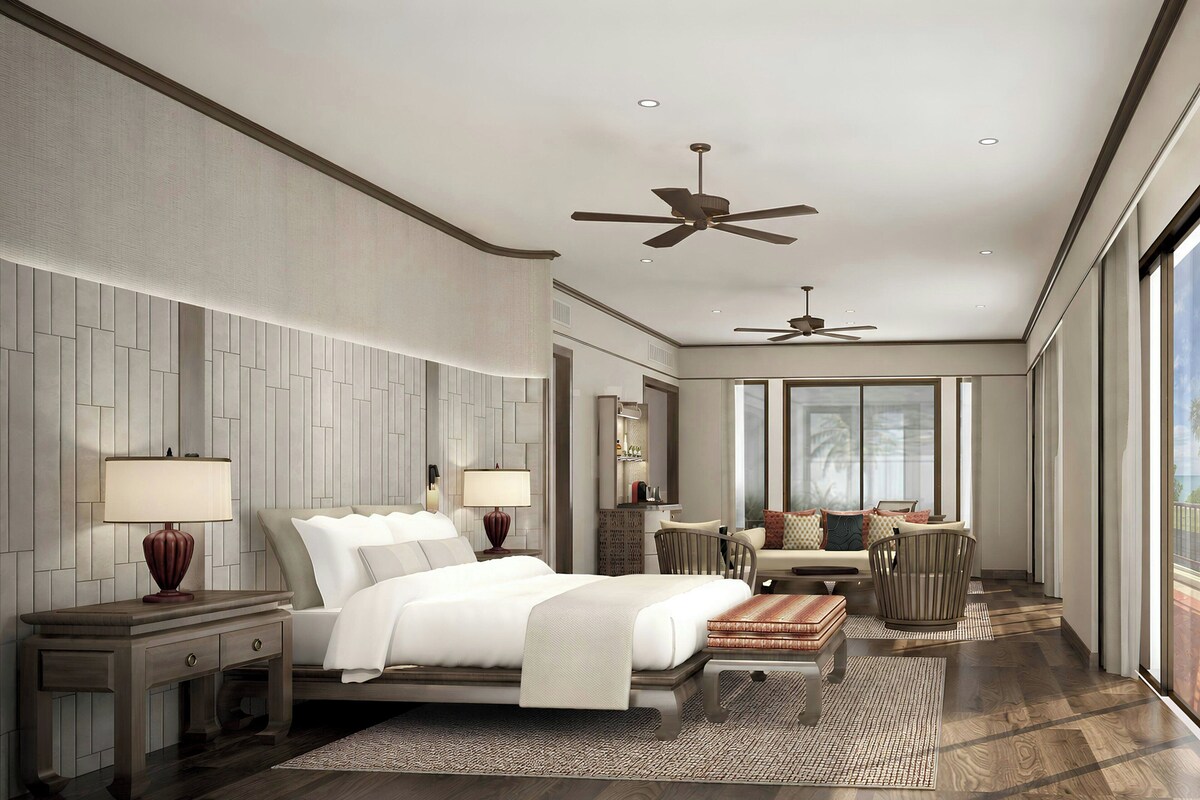 A modern hotel room with a large bed, two bedside tables, a desk, a chair, a sofa, and a ceiling fan.