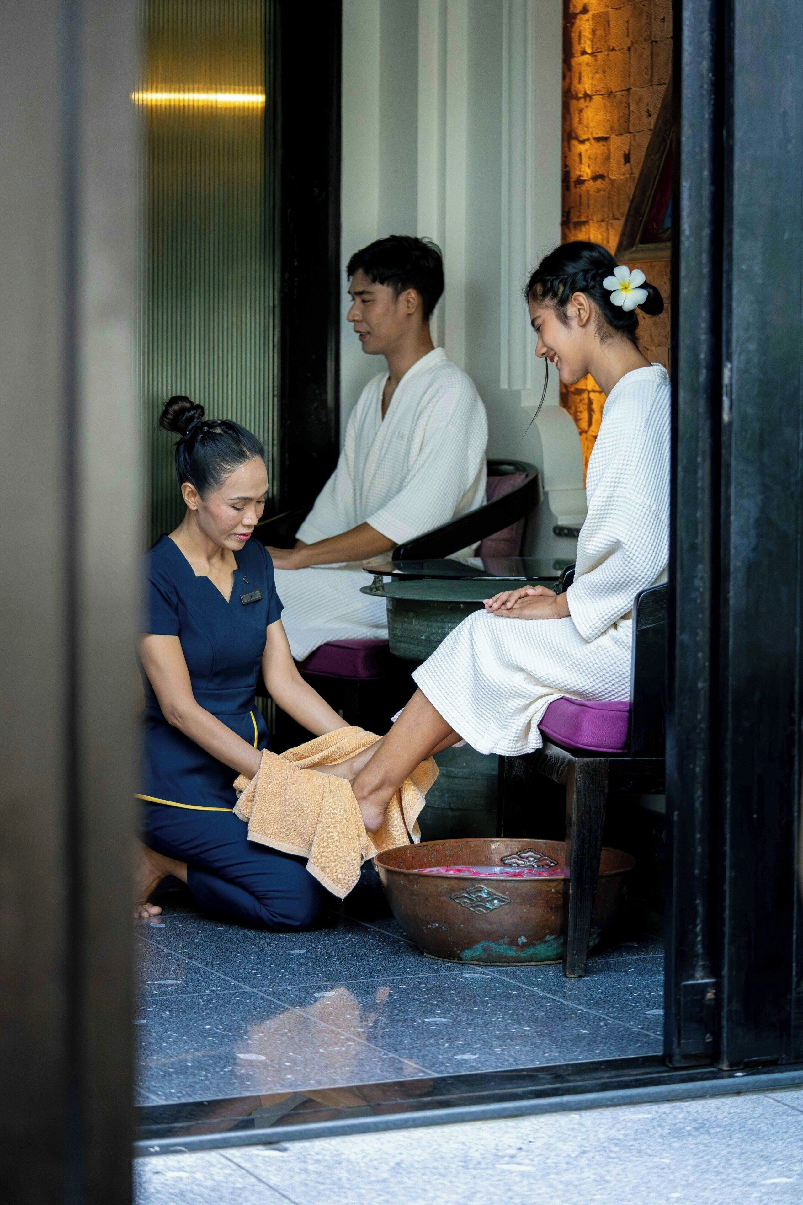 A person receiving a foot massage in a room with a tiled floor and a wooden bench.
