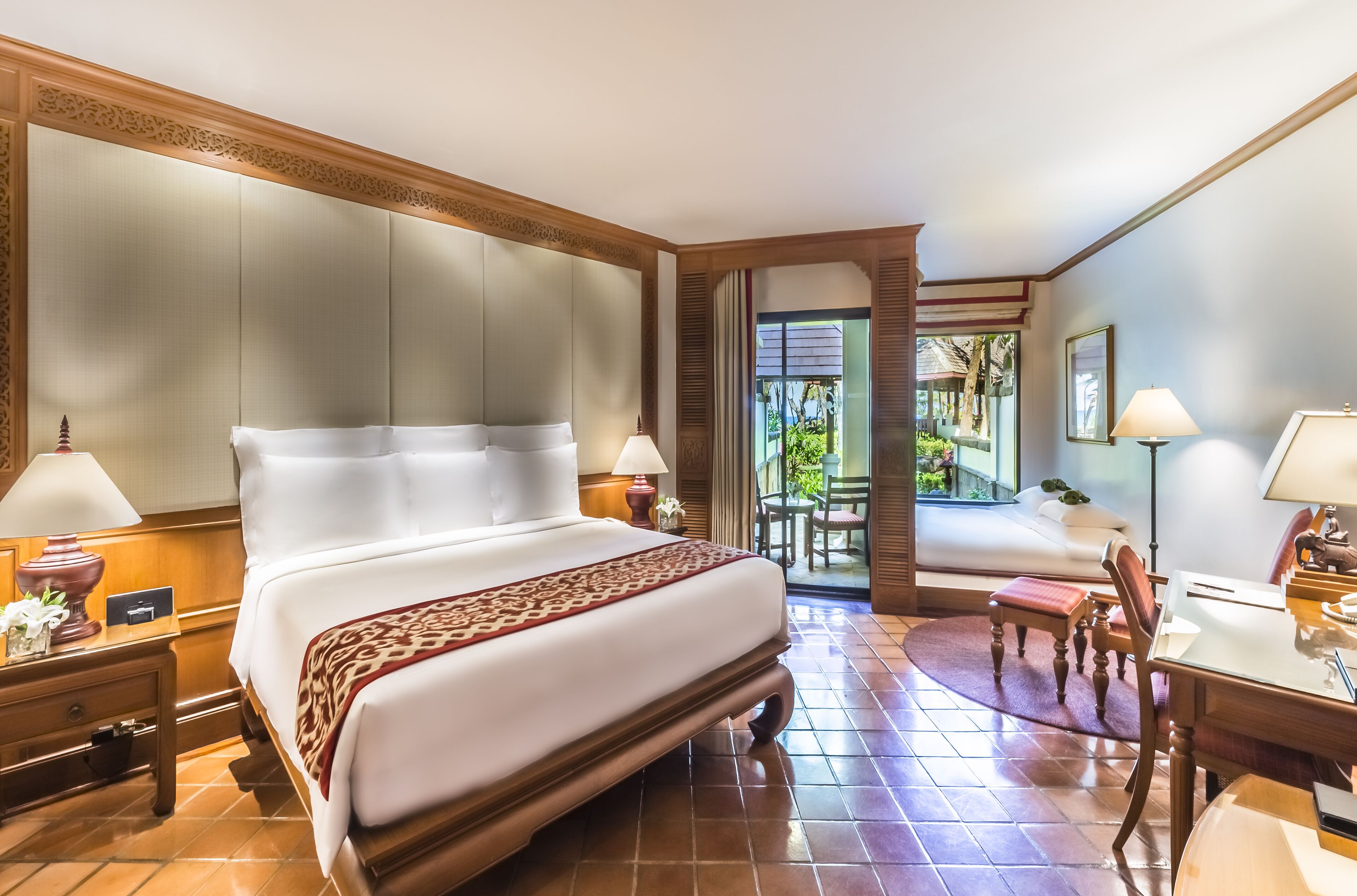A hotel room with a large bed, two bedside tables with lamps, a desk with a chair, and a view of the outdoors.