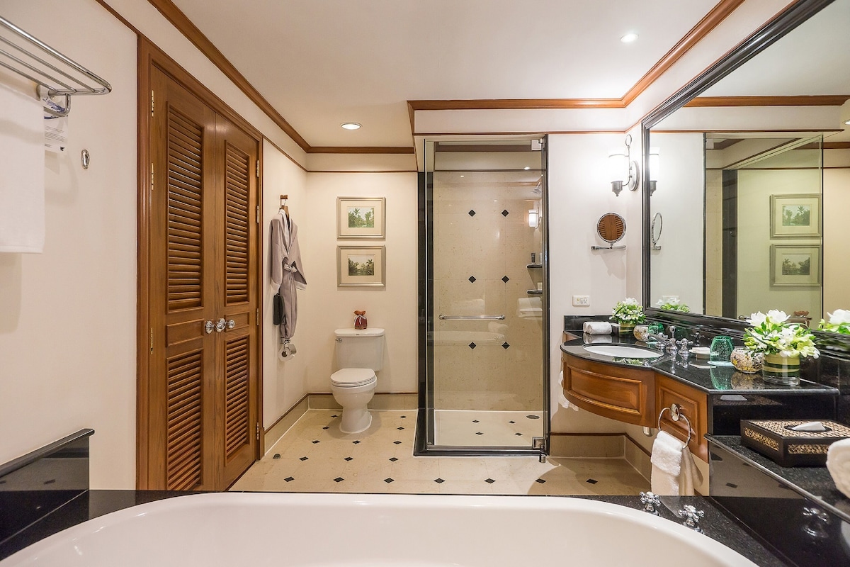 A modern bathroom with a bathtub, a glass-enclosed shower, wooden doors, and a vanity with a mirror.