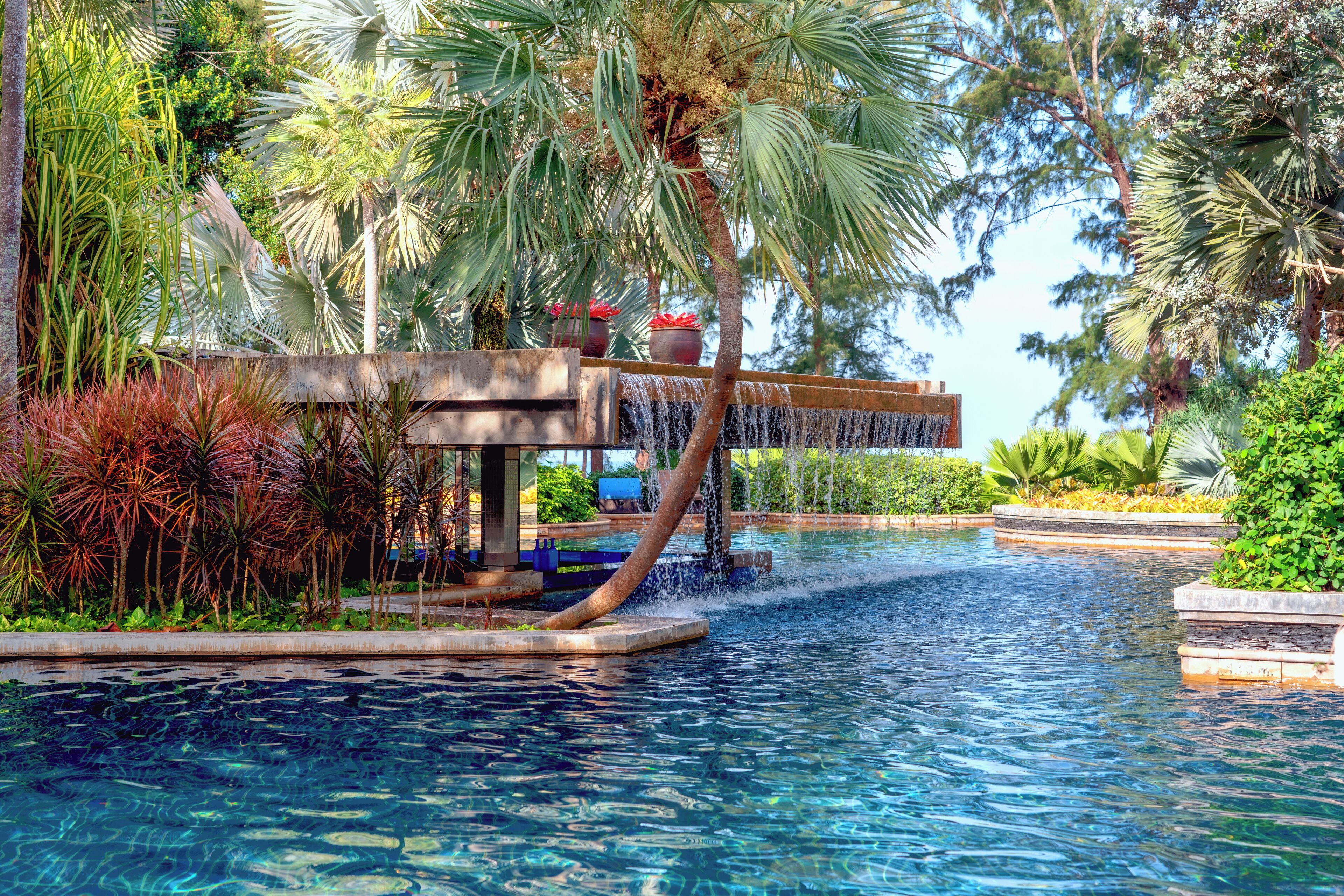 A pool area with a waterfall feature, surrounded by tropical plants and palm trees.