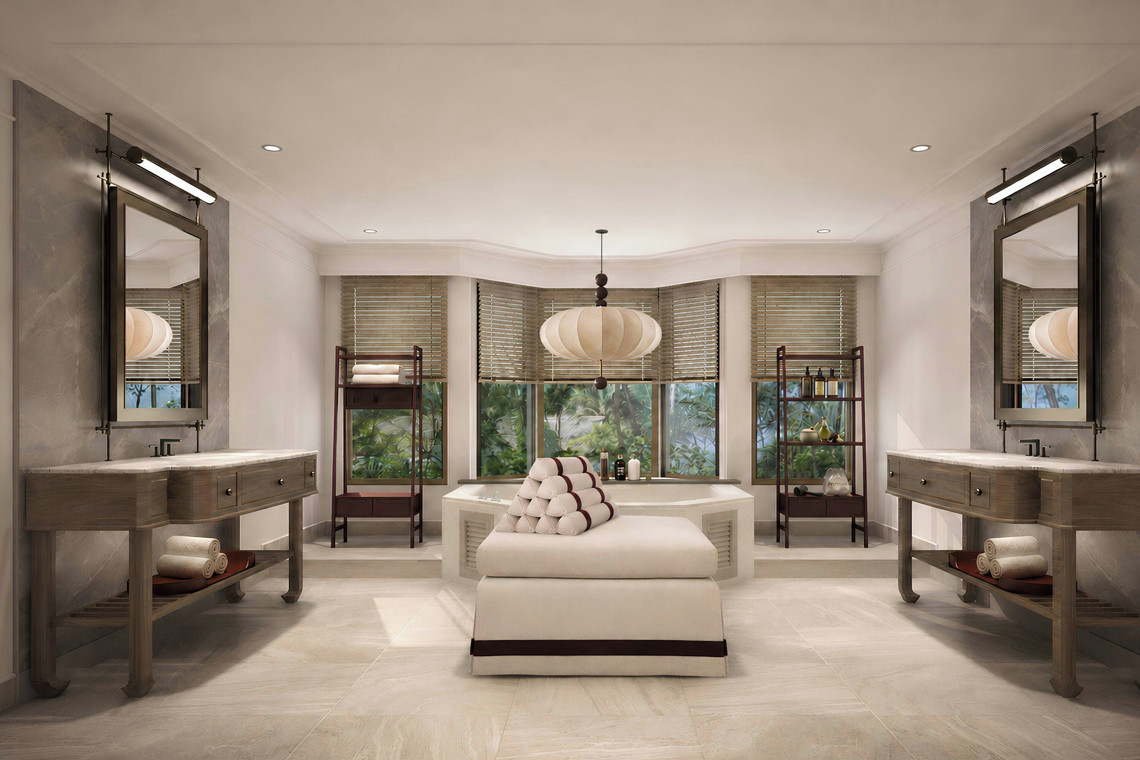 A modern bathroom with two sinks, a large mirror, a central seating area, and a view of greenery through the windows.