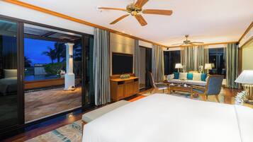 Una habitación de hotel con una cama grande, televisión, sofá, sillón y ventilador de techo.