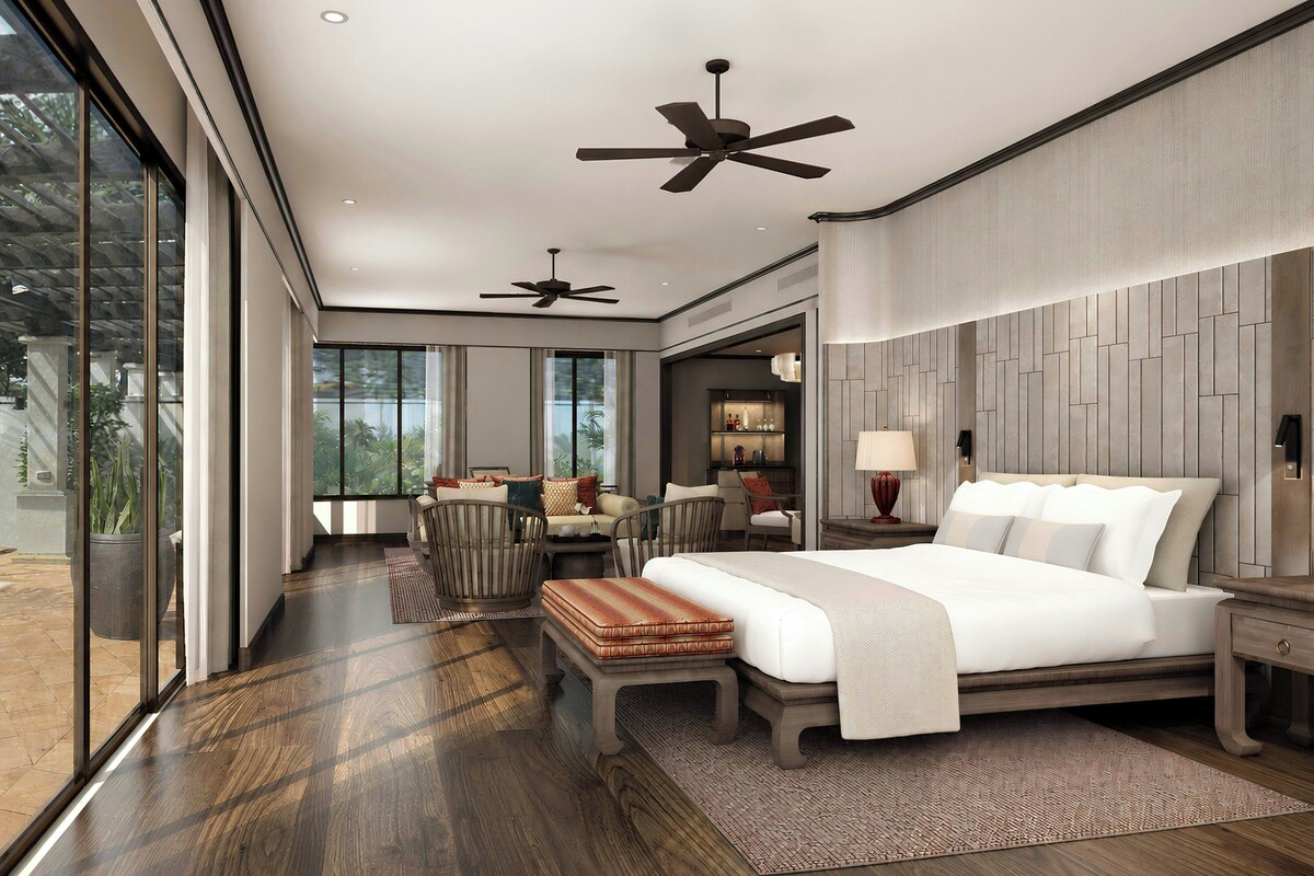 A modern bedroom with a large bed, two ceiling fans, a dining area with a table and chairs, and a view through large windows.