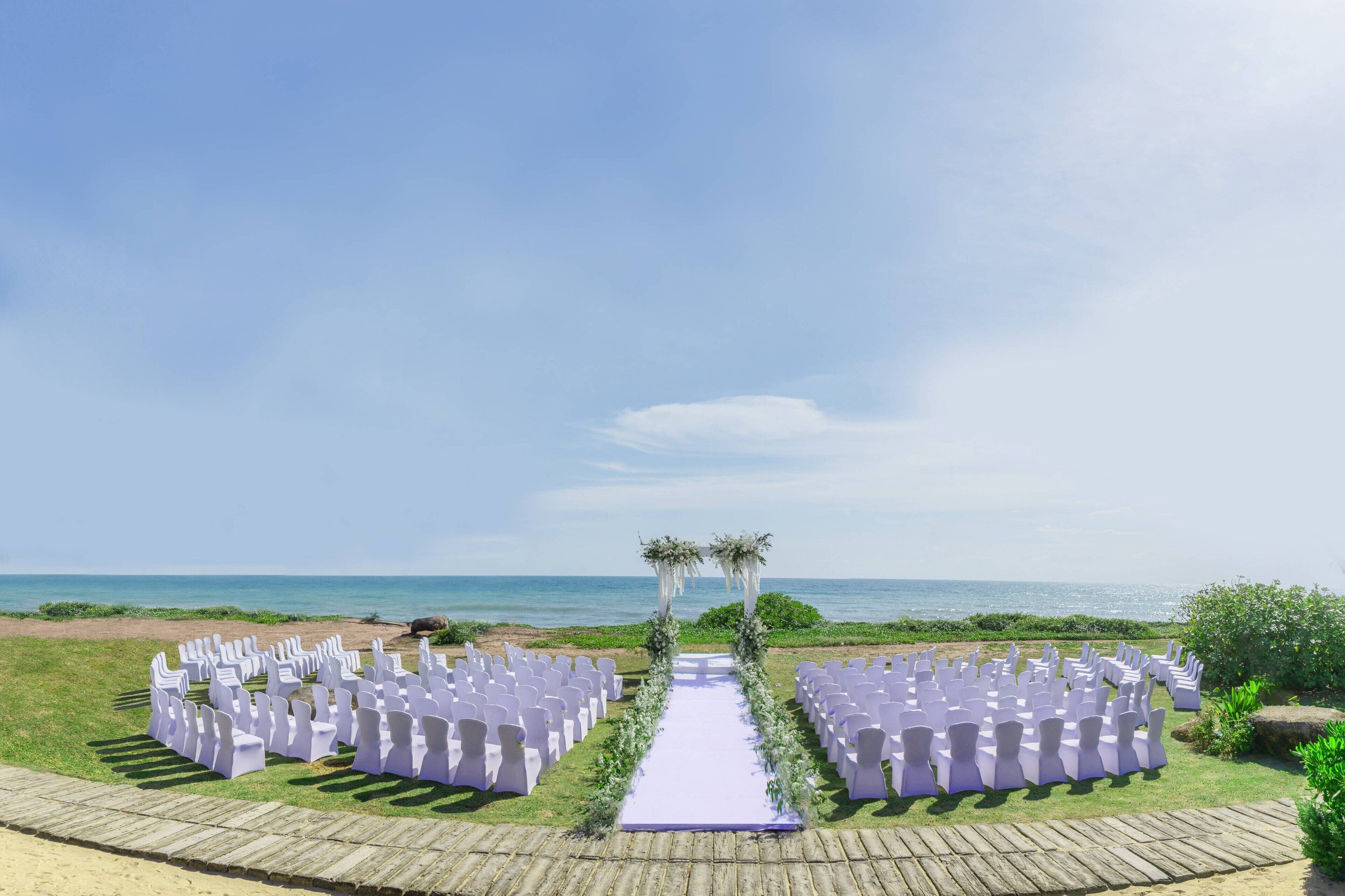 Montaje para una boda al aire libre con una terraza de madera, sillas blancas y un arco floral.