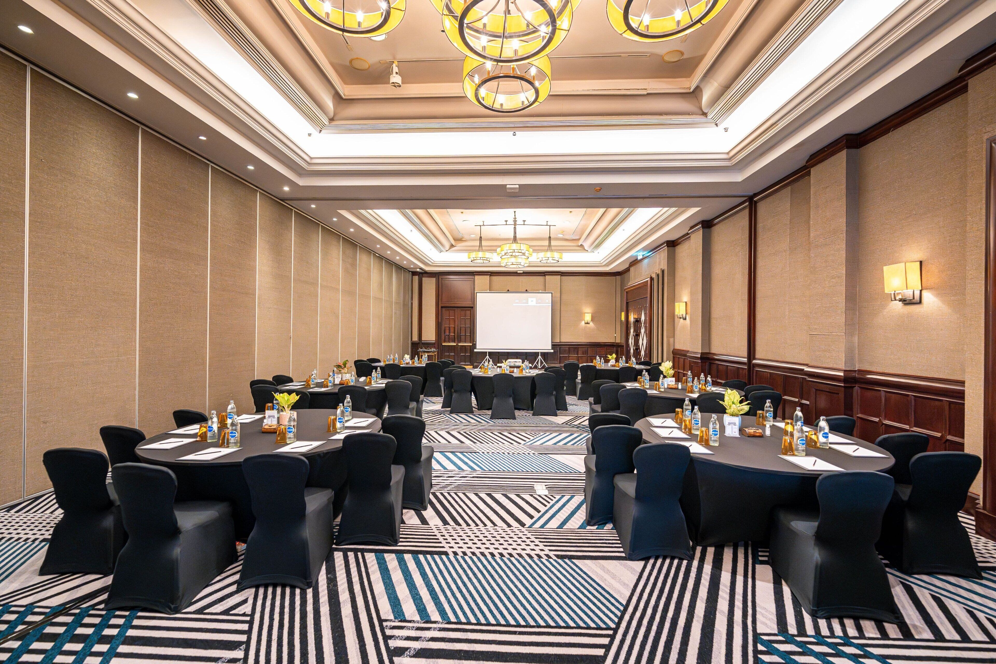 A conference room with round tables, black chairs, and a projector screen.