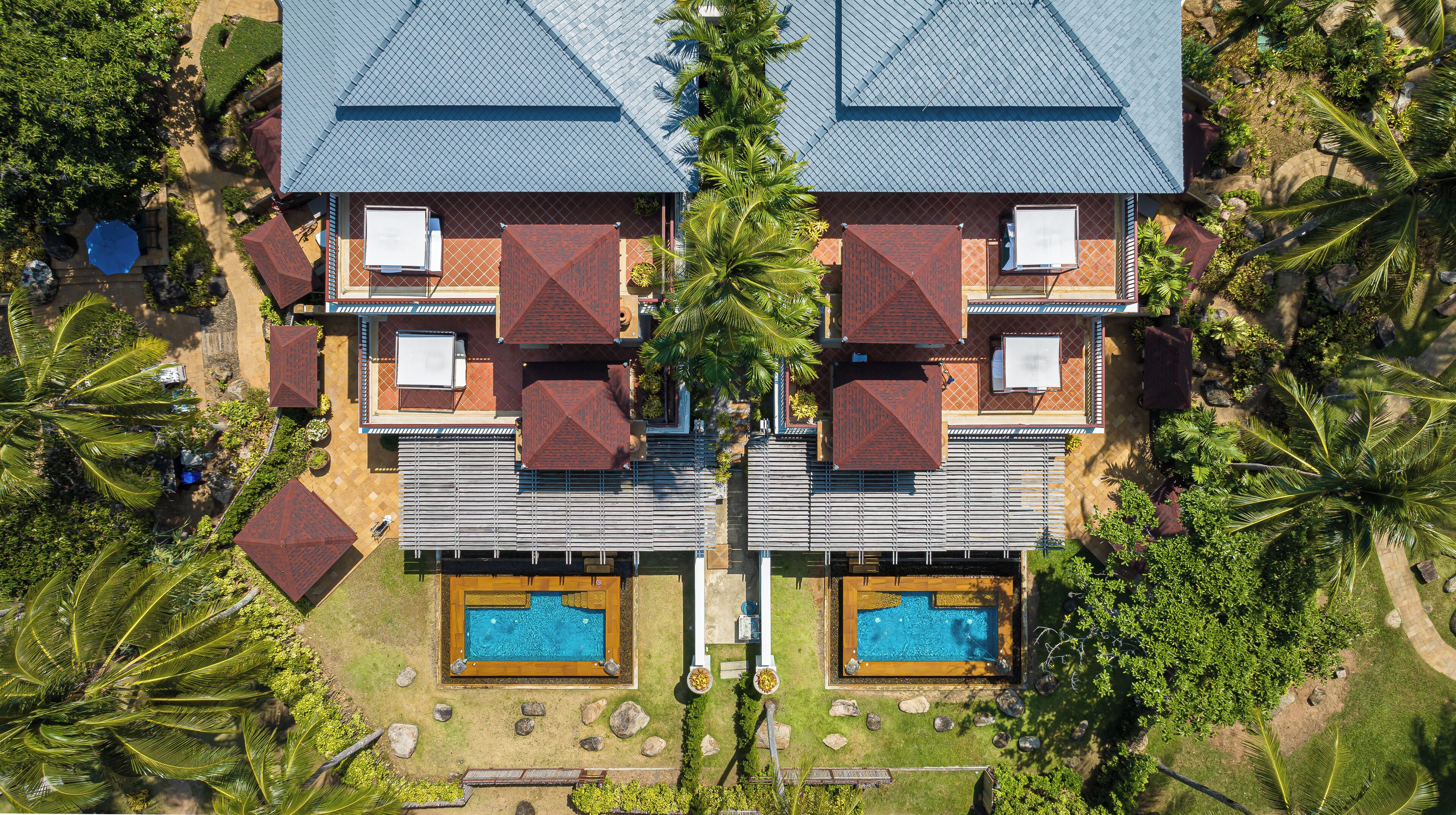 Un bâtiment symétrique doté de deux piscines, entouré de palmiers et d’une pelouse bien entretenue.
