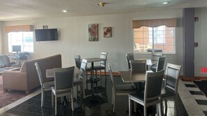 A dining area with a high table and chairs, a sofa, a flat-screen TV, and artwork on the walls.