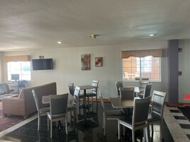 A dining area with a high table and chairs, a sofa, a flat-screen TV, and artwork on the walls.