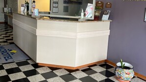A reception area with a check-in counter, a check-out counter, and a reception desk. There are framed certificates and a welcome sign on the wall.