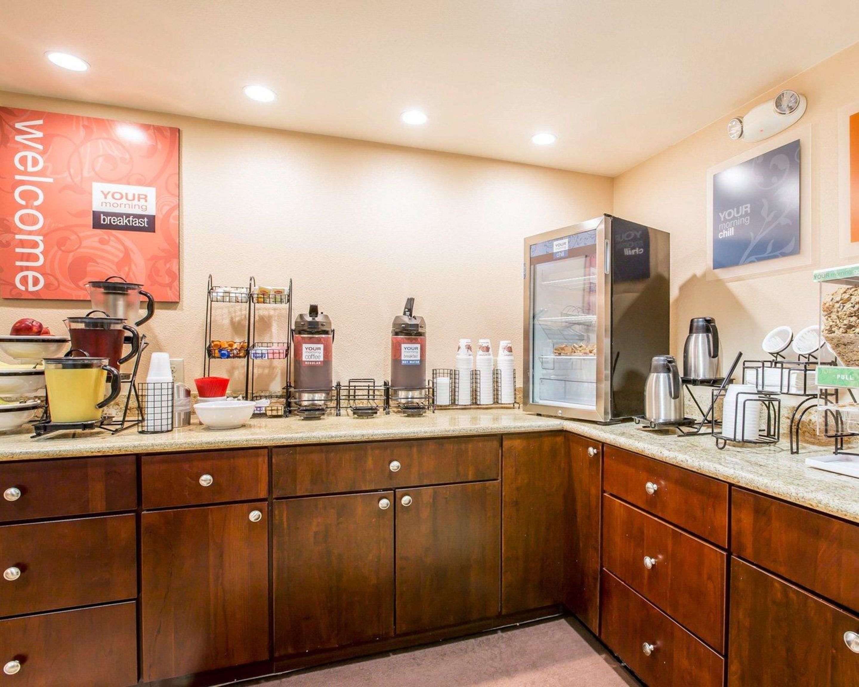 Zona de desayuno de hotel con máquinas de café, un refrigerador y una estación para café.
