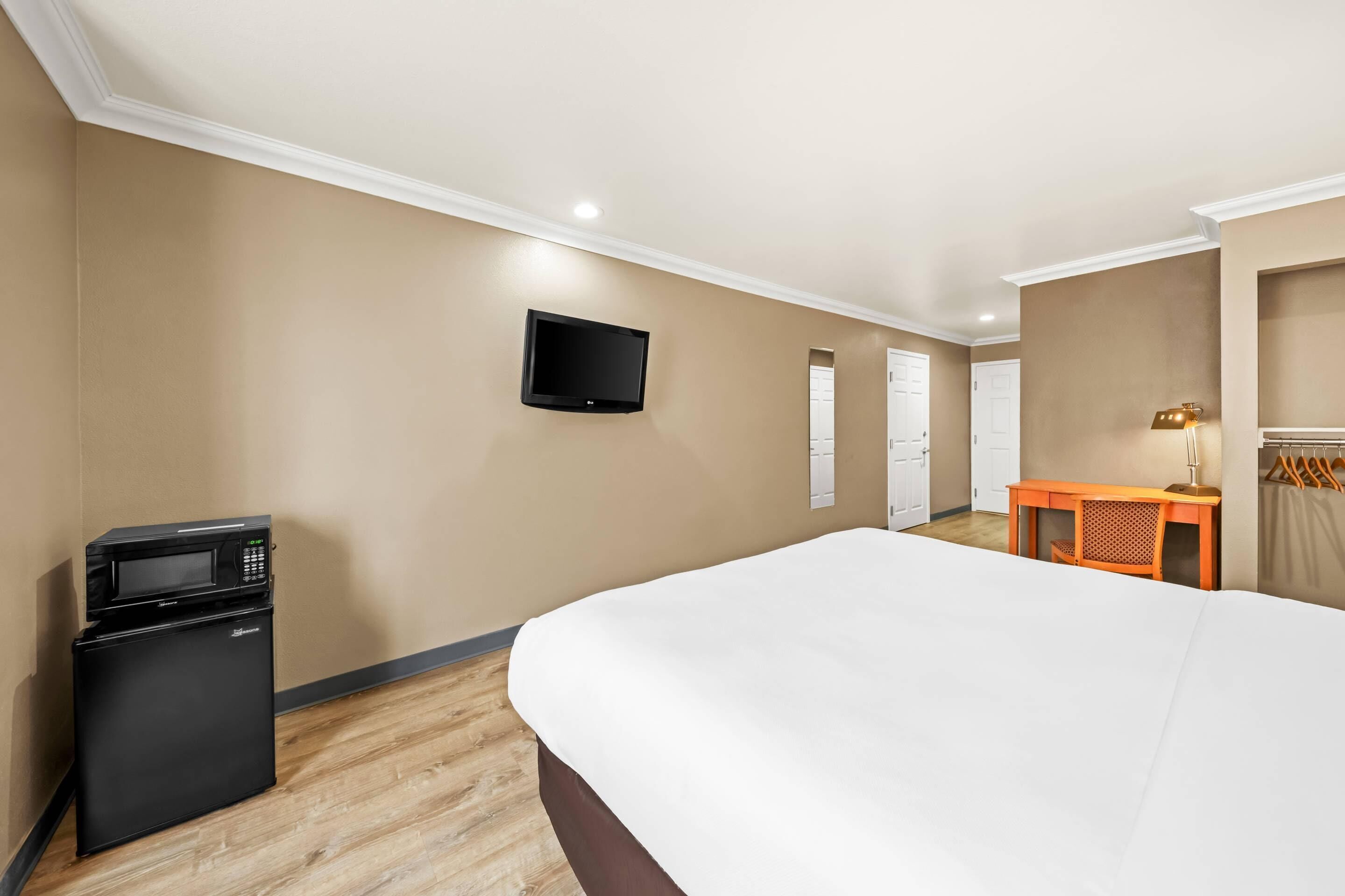 A hotel room with a bed, a desk, a television, and a refrigerator.