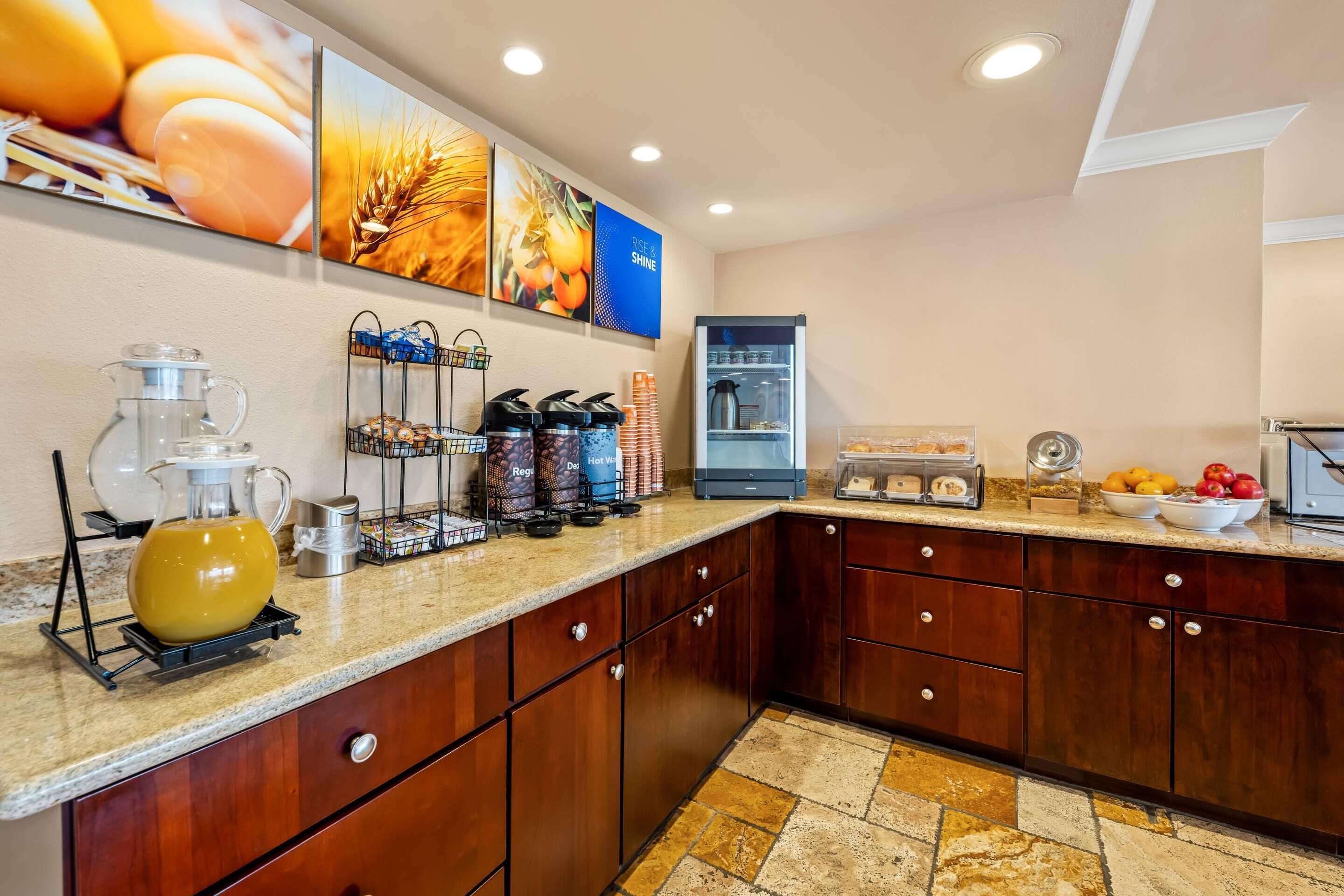 A modern kitchen with a granite countertop, wooden cabinets, a coffee station, and a refrigerator.