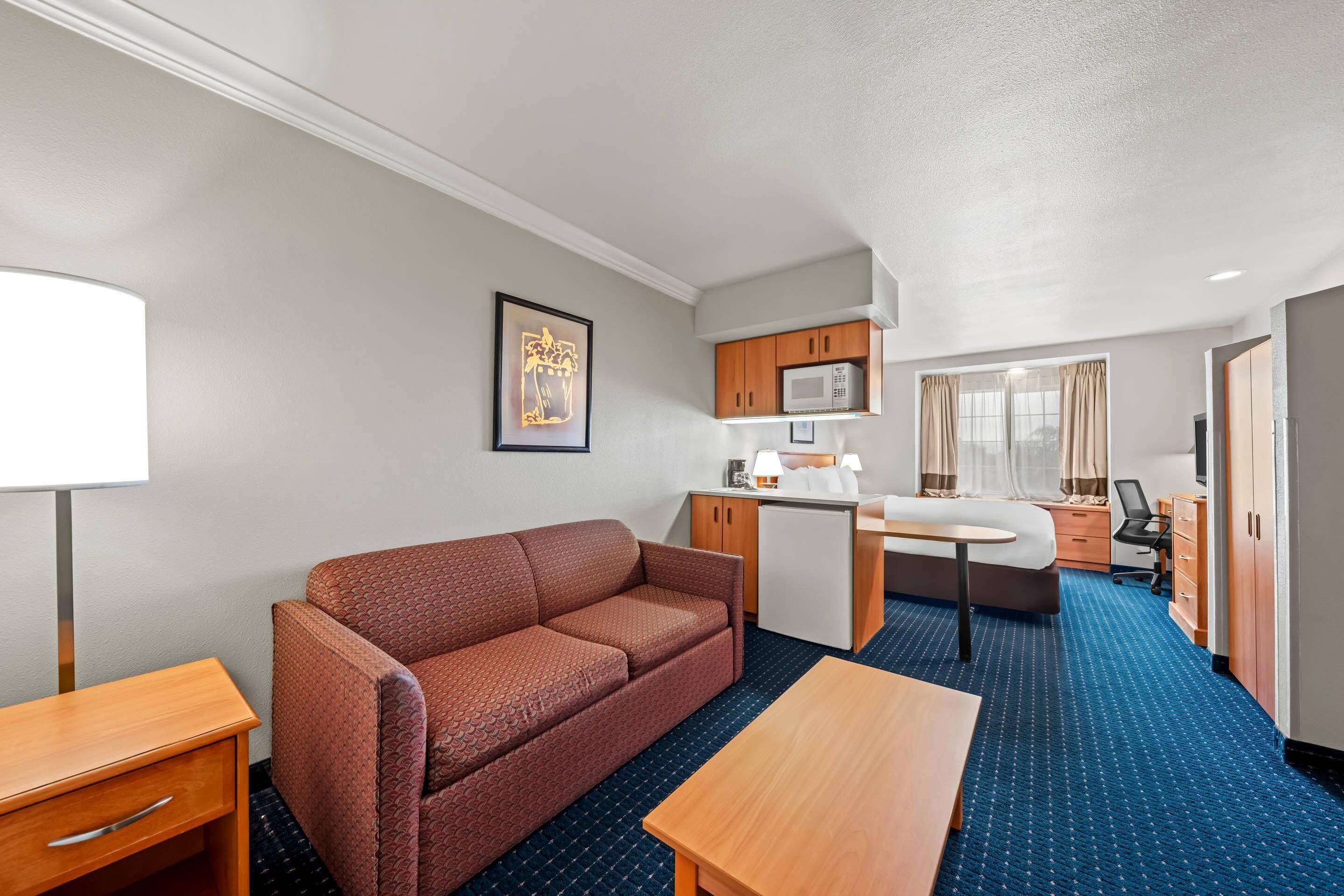 Een compacte hotelkamer met een bank, een tafeltje, een kitchenette en een bed.