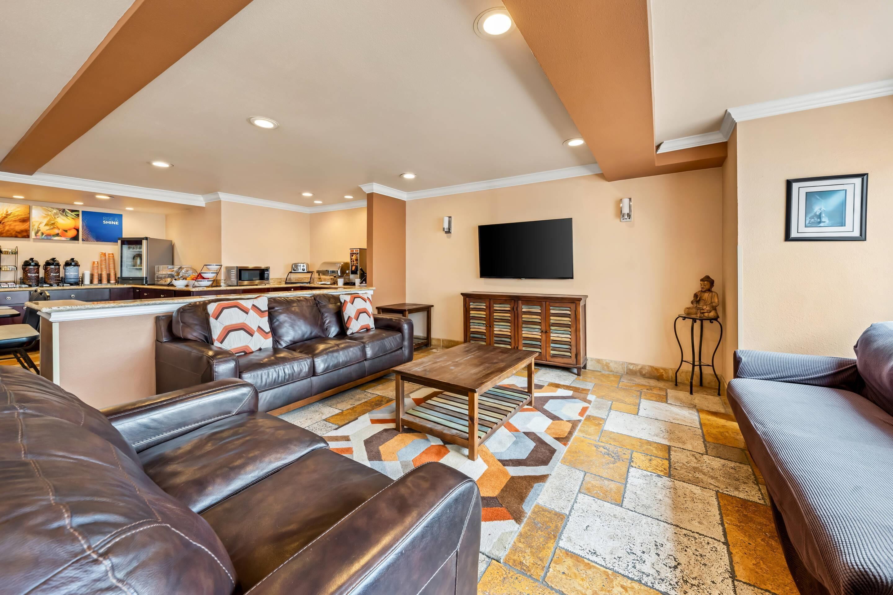 A spacious living area with leather sofas, a coffee table, a TV, and a kitchen area with a refrigerator and microwave.
