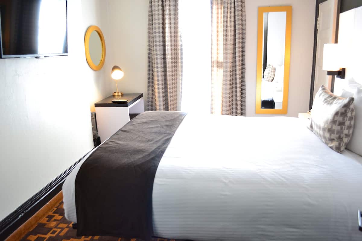Una habitación de hotel con una cama, una mesita de noche con lámpara, un espejo y cortinas.