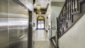 A hallway with a herringbone floor, a staircase with dark balusters, and a large chandelier. - Adante Hotel (San Francisco)