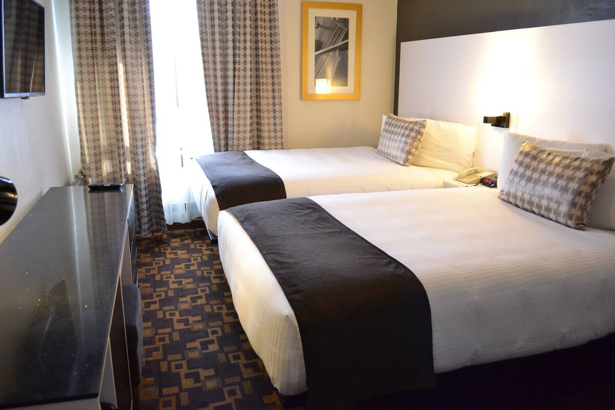 Una habitación de hotel con dos camas, un escritorio y una alfombra estampada.