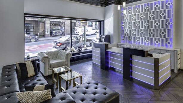 A modern reception area with a leather sofa, a glass coffee table, and a reception desk with illuminated panels. - Adante Hotel (San Francisco)