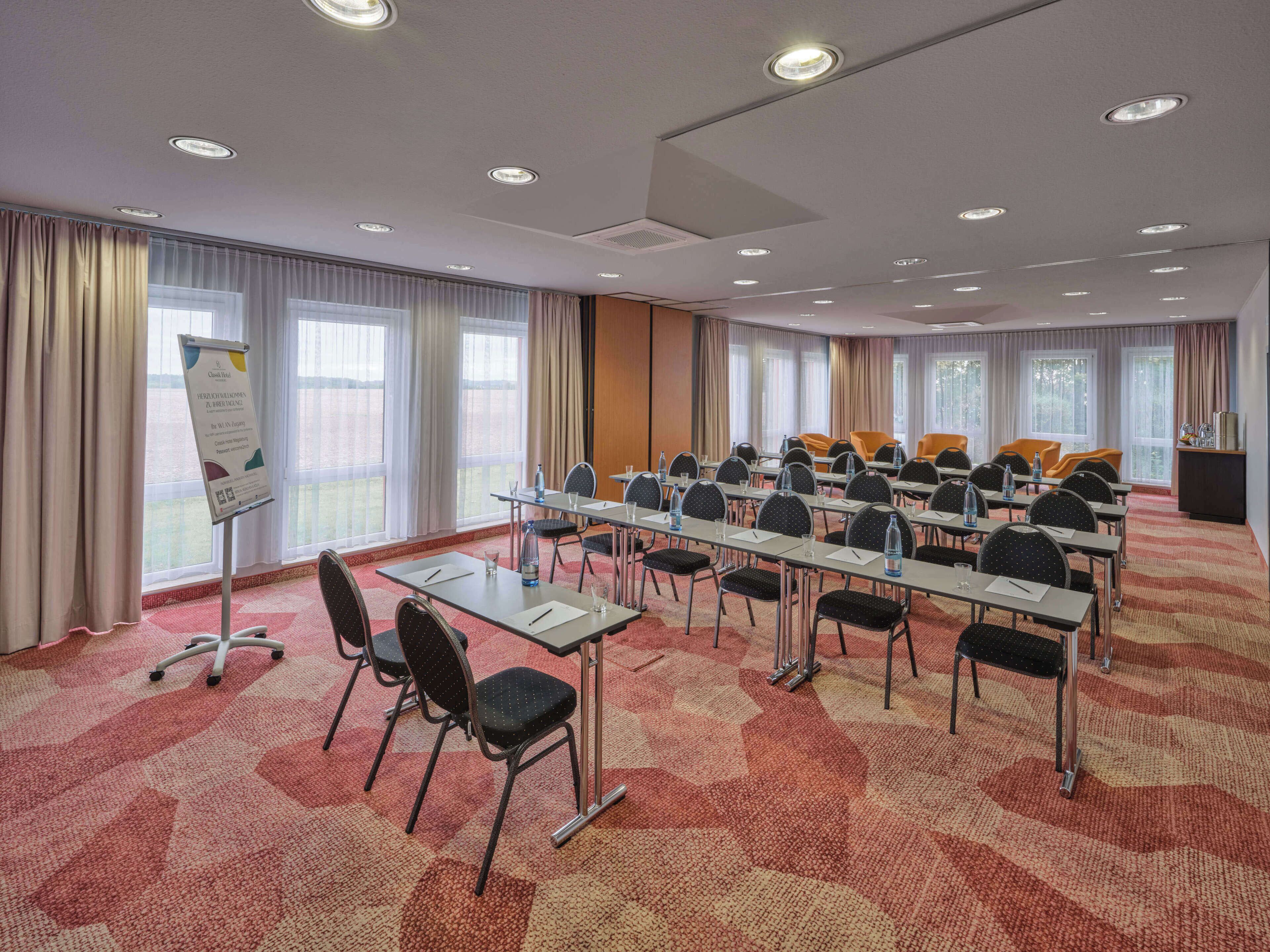 Una sala de conferencias con mesas, sillas y una pizarra para presentaciones.