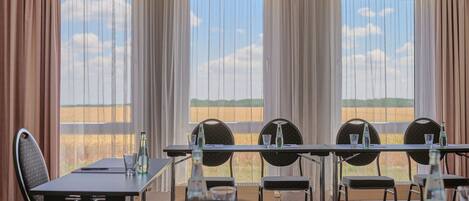 Una sala de conferencias con una larga mesa, sillas y ventanas grandes con cortinas.