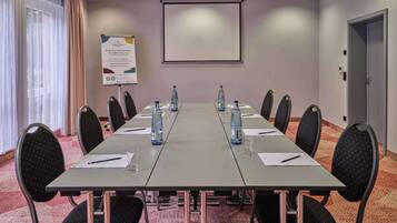 A conference room with a long table, chairs, water bottles, and a projector screen.
