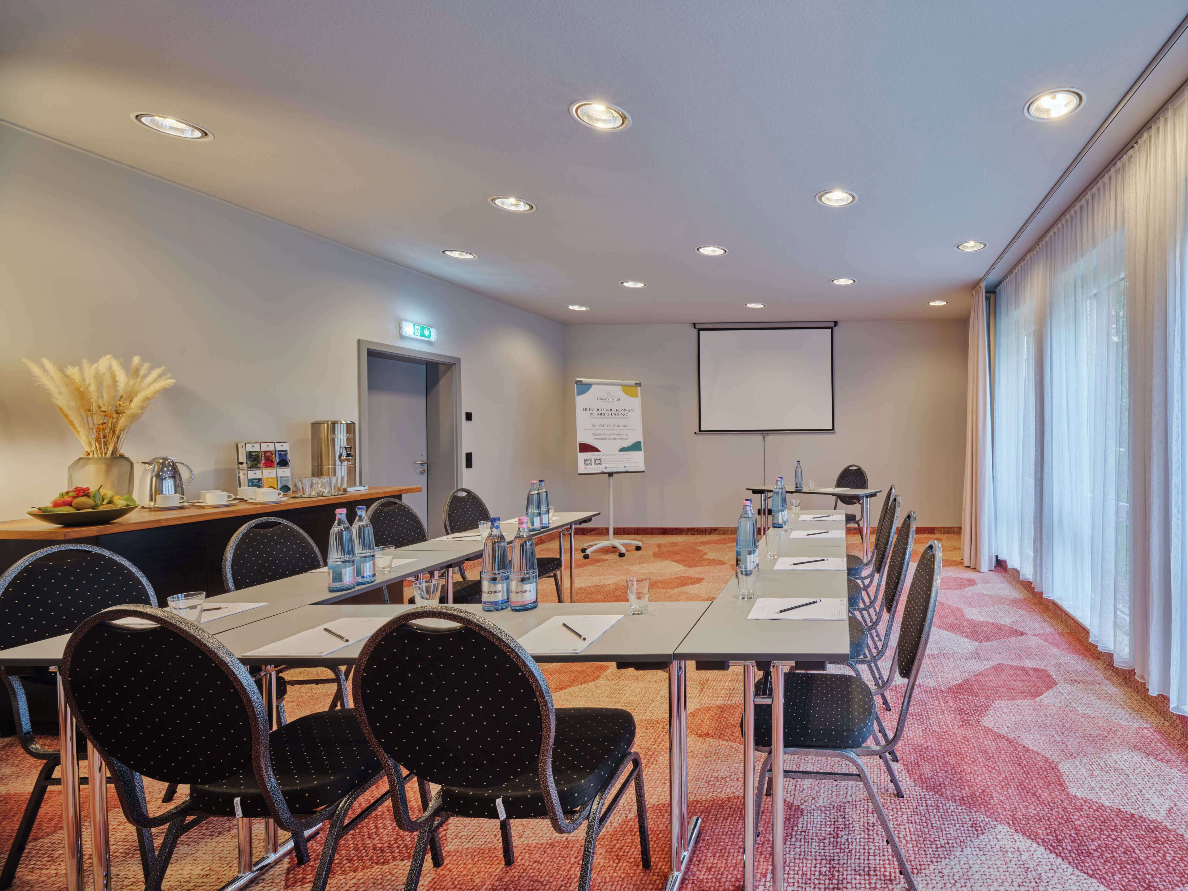 A conference room with a long table, chairs, water bottles, a projector screen, and a whiteboard.