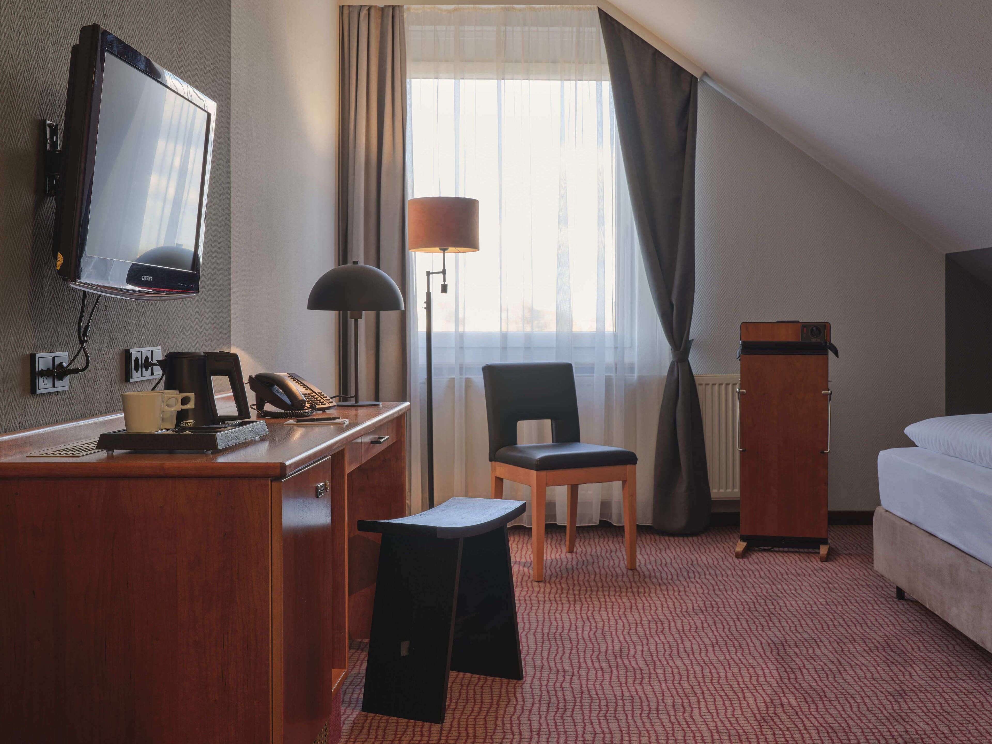 Une chambre d’hôtel équipée d’un bureau, d’une chaise, d’un lit, d’une télévision, d’une lampe et offrant une vue sur l’extérieur.