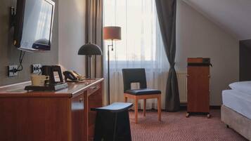 Une chambre d’hôtel équipée d’un bureau, d’une chaise, d’un lit, d’une télévision, d’une lampe et offrant une vue sur l’extérieur.