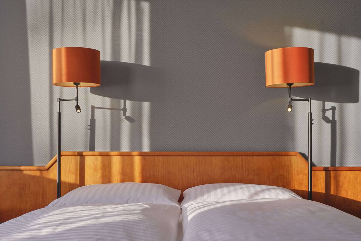 Una cama bien hecha con dos lámparas fijadas a la pared a cada lado.