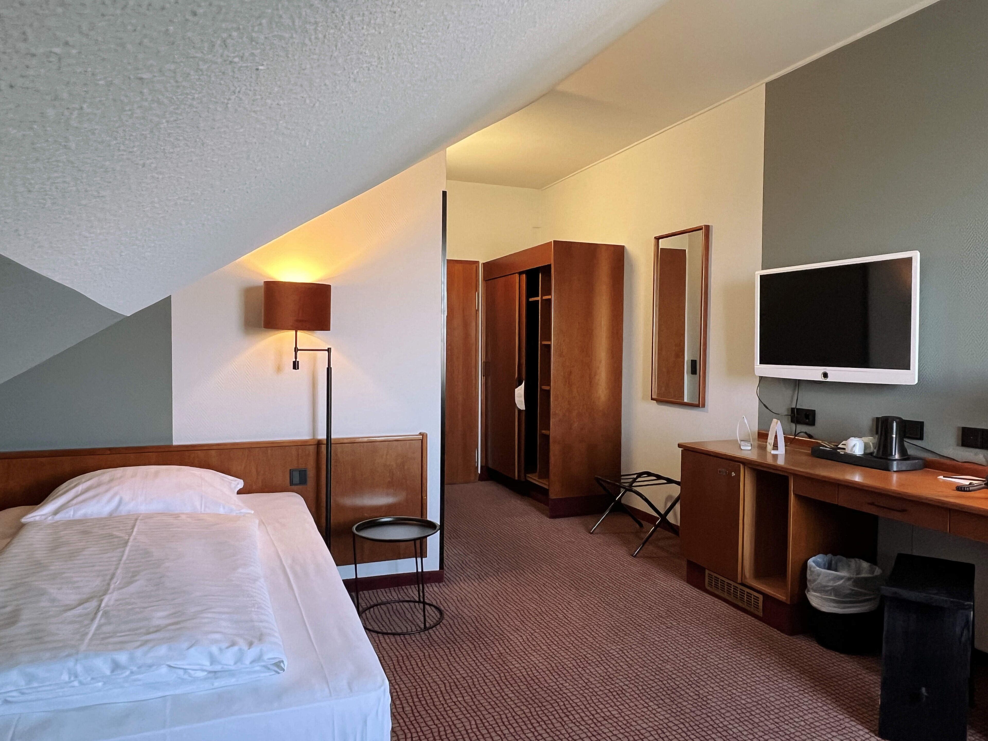 Una habitación de hotel con una cama, un escritorio, un televisor y un armario.