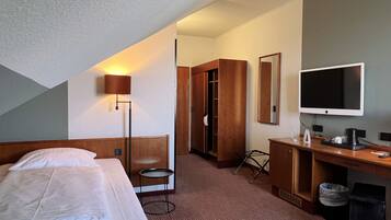 Una habitación de hotel con una cama, un escritorio, un televisor y un armario.