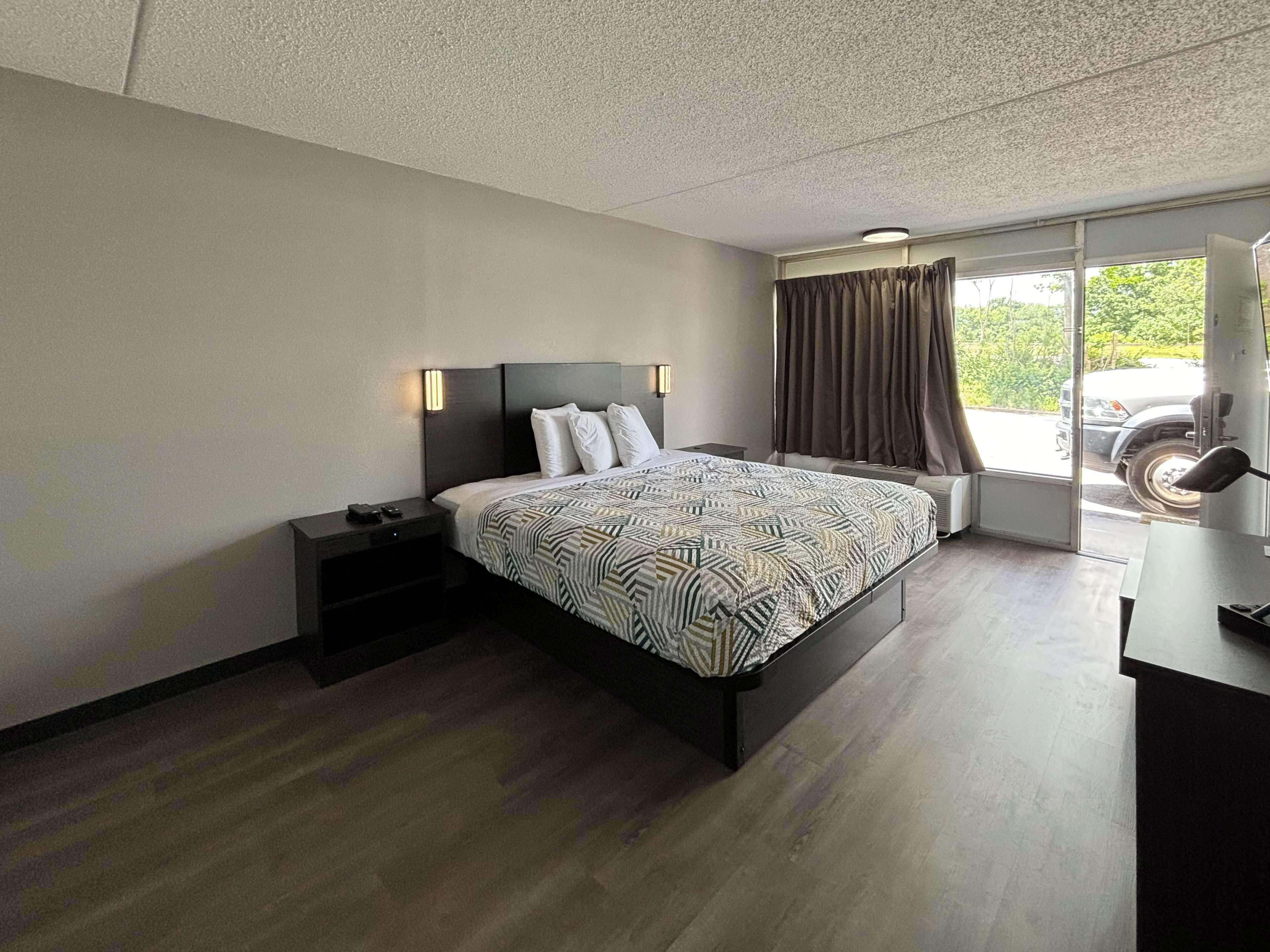 A modern hotel room with a large bed, a nightstand, a desk, and a window with curtains.