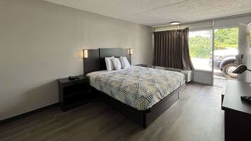A modern hotel room with a large bed, a nightstand, a desk, and a window with curtains.