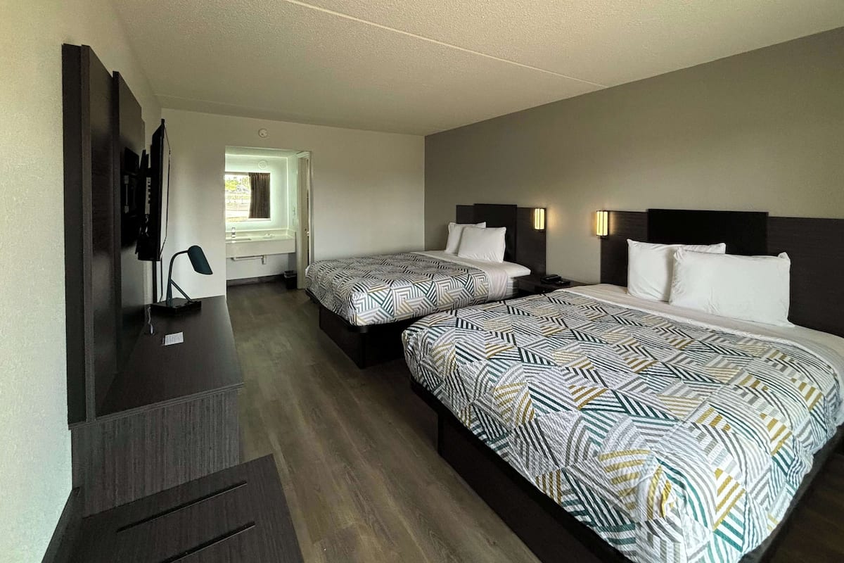 A hotel room with two beds, a desk, a TV, and a window with a view.