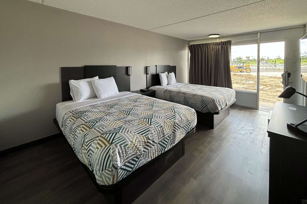 A hotel room with two beds, a desk, and a large window with curtains.