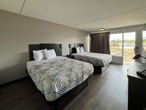Habitación de hotel con dos camas, un escritorio y un ventanal grande con cortinas.