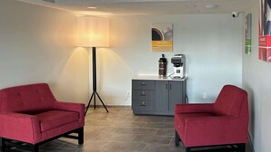 A room with two red chairs, a floor lamp, a coffee machine, and a cabinet. - Motel 6 Richmond, KY – EKU Campus Area (Richmond)