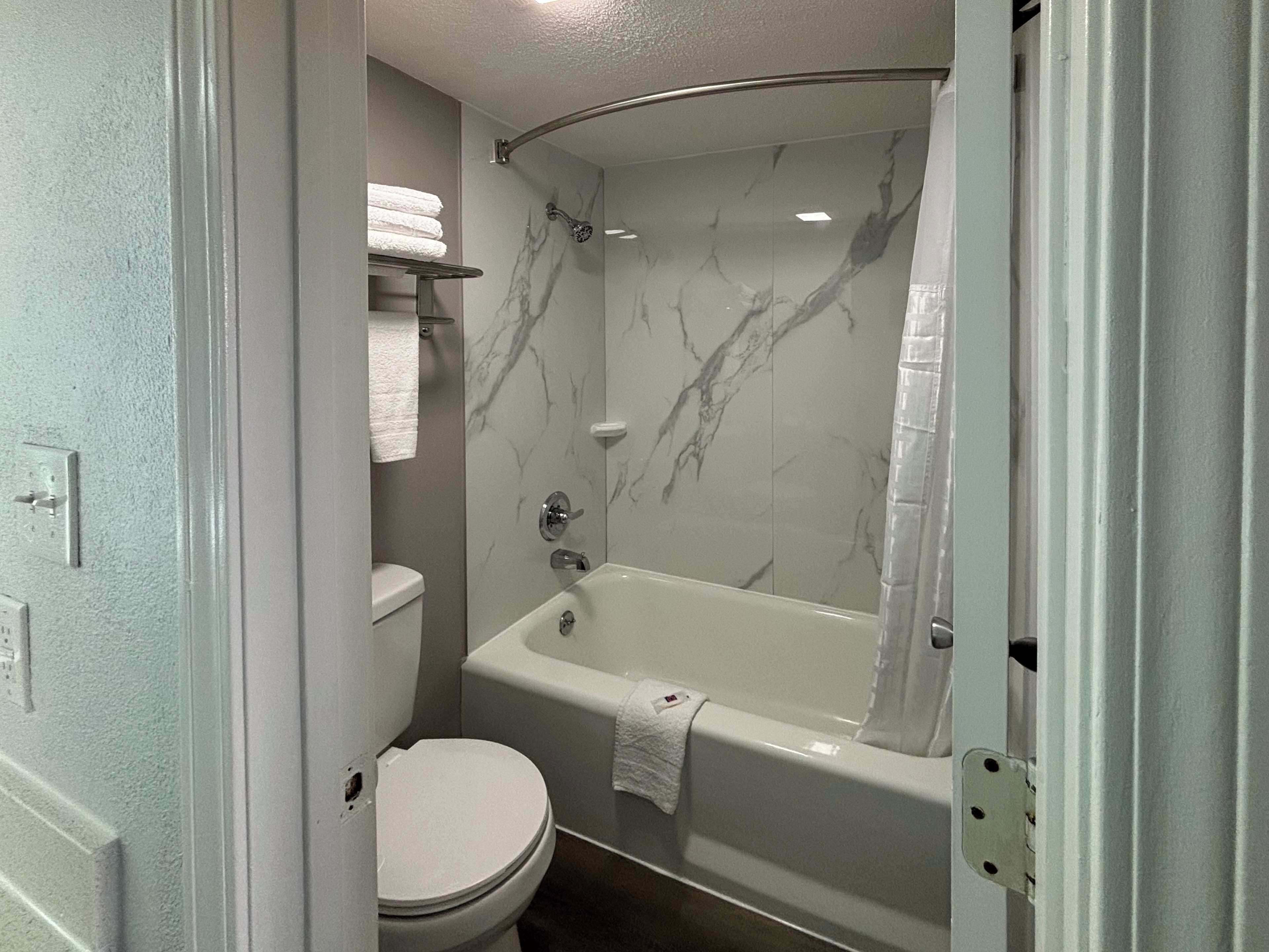 Une salle de bain avec des toilettes blanches, une baignoire avec un rideau de douche et des murs en marbre.