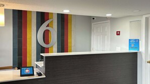 A reception desk with a large number '6' sign, a digital display, and a QR code sign on the wall. - Motel 6 Richmond, KY – EKU Campus Area (Richmond)