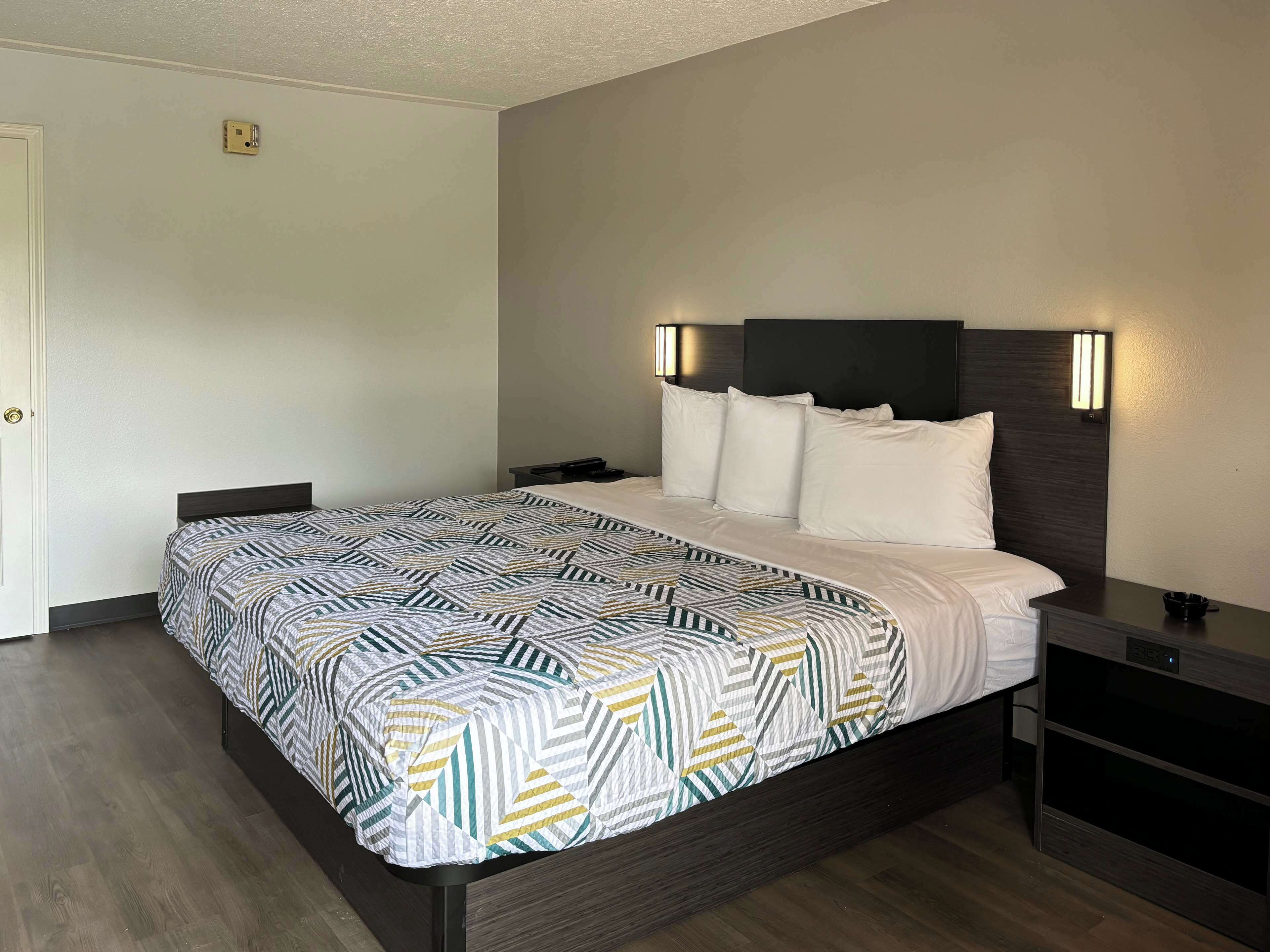 Una habitación de hotel con cama, mesitas de noche y una lámpara fijada en la pared.