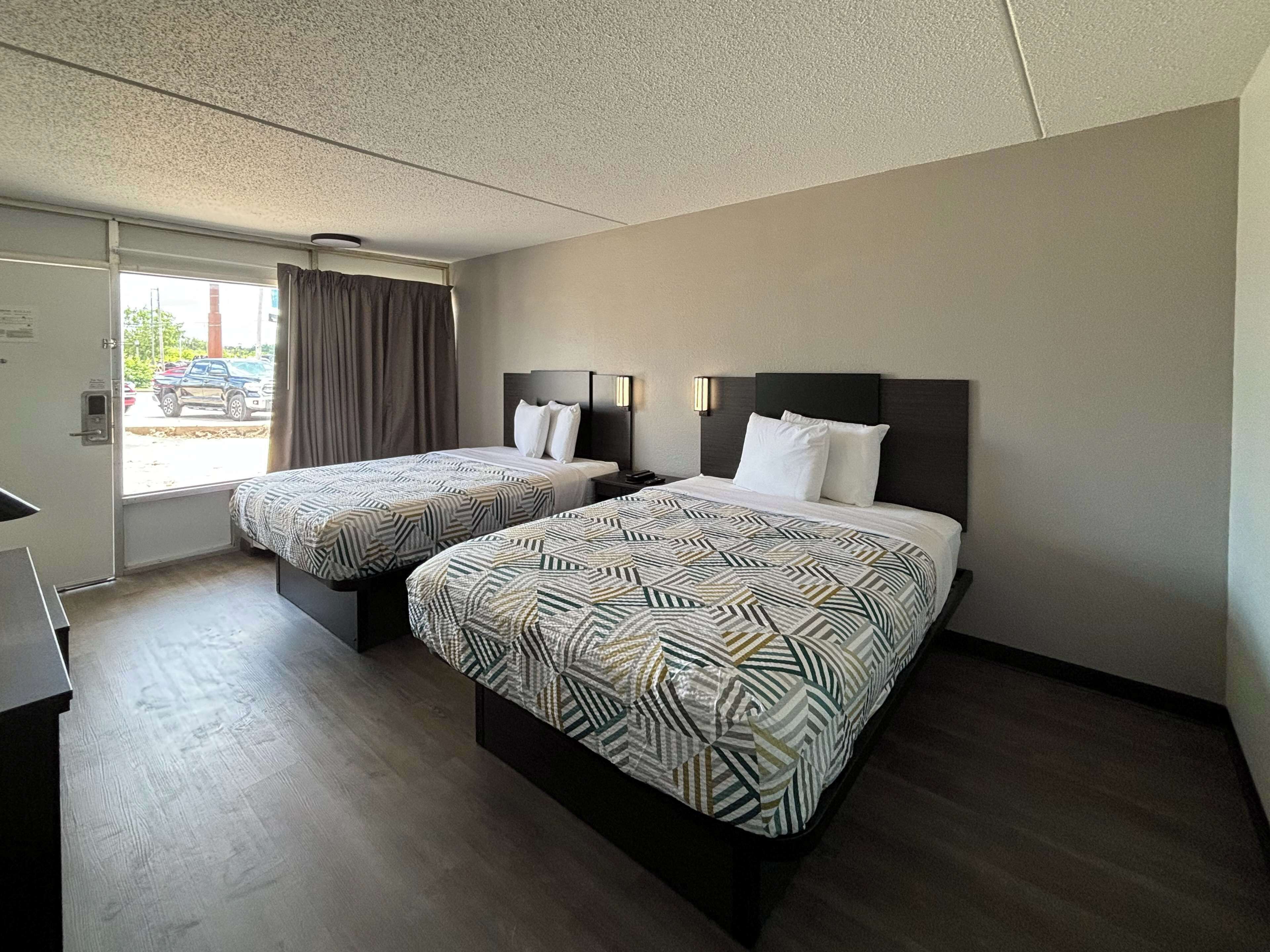 A hotel room with two beds, a desk, and a window with curtains.