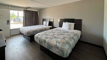 A hotel room with two beds, a desk, and a window with curtains.