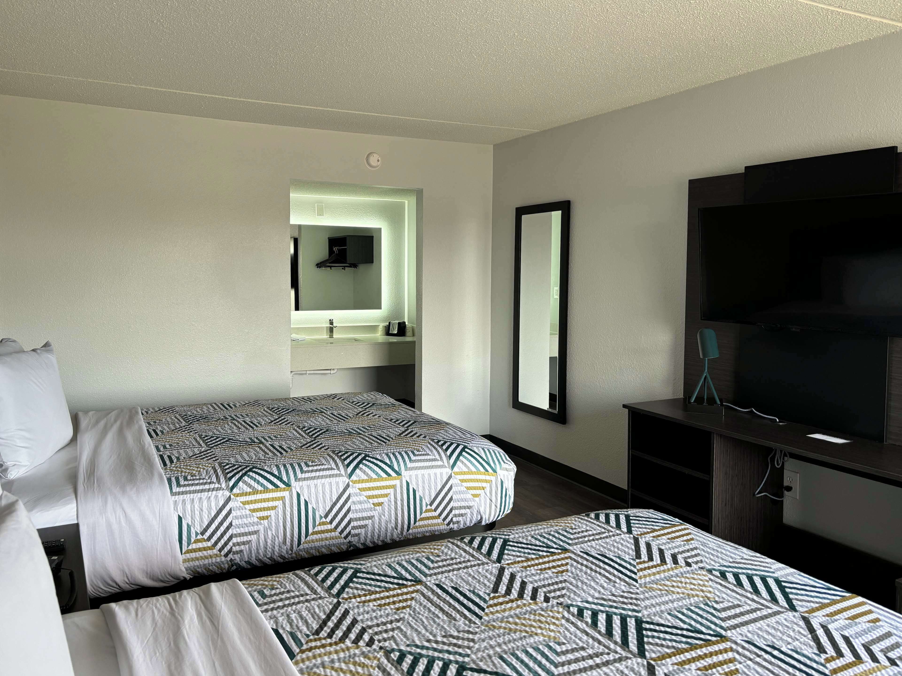 Habitación de hotel con dos camas, un espejo grande, un televisor y un escritorio pequeño.