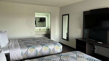 Habitación de hotel con dos camas, un espejo grande, un televisor y un escritorio pequeño.