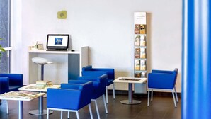 Un área de espera moderna con sillas azules, una computadora portátil sobre un escritorio y un mueble con revistas.
