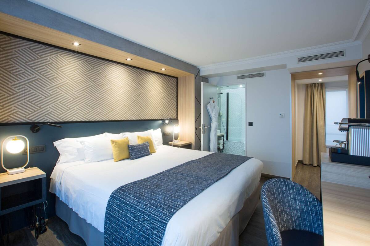 Una habitación de hotel moderna con una cama grande, mesitas de noche, un espejo y un rincón de descanso.
