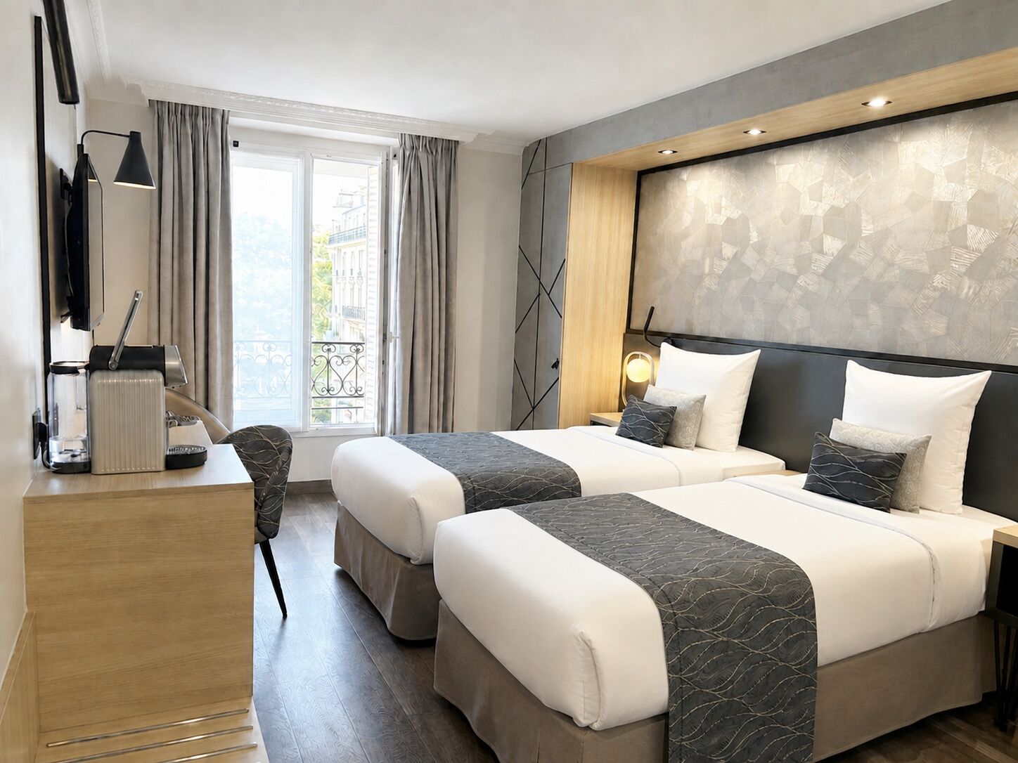 Habitación de hotel con dos camas, un escritorio con cafetera, una silla y vista a la ciudad.