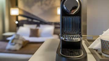 Une machine à café est posée sur une table dans une chambre d’hôtel, avec un lit et un tableau en arrière-plan.